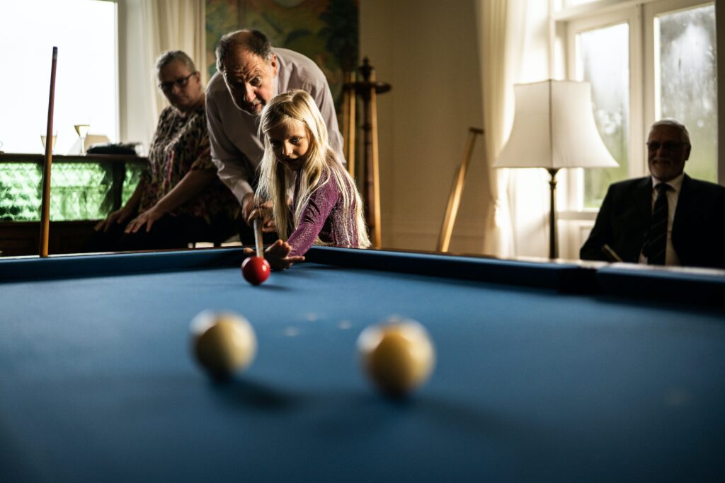 Grandpa teaching his granddaughter how to hold a pool stick