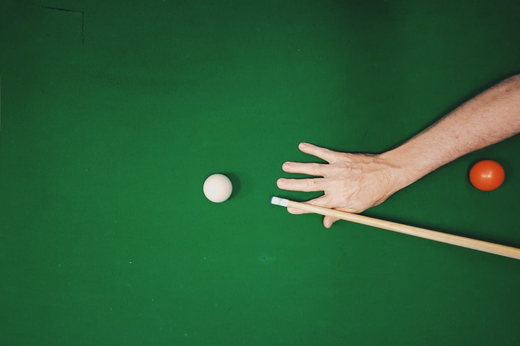Player aiming at a cue ball on a pool table with green felt color