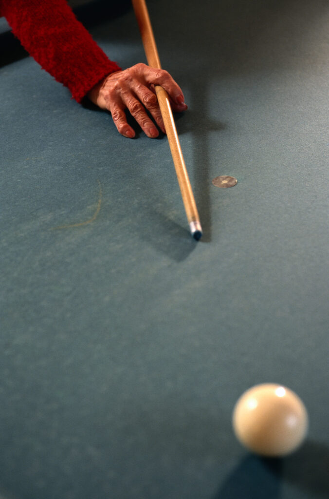 Person holding a pool cue aiming for a ball