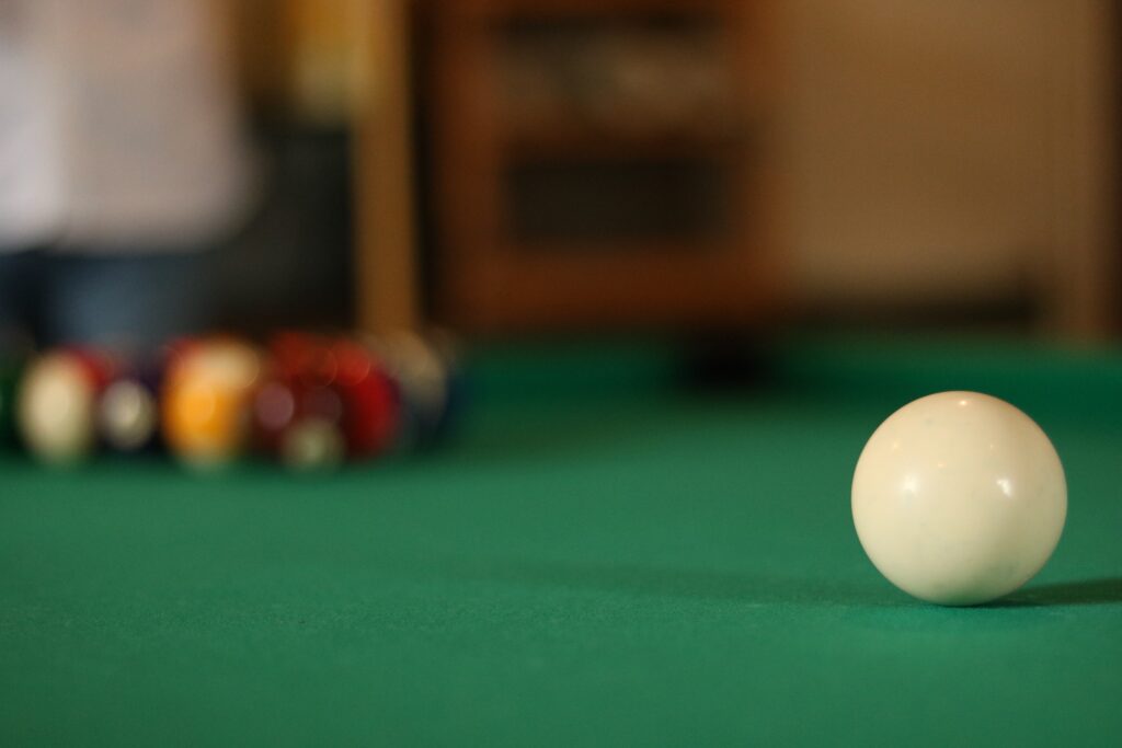 A white cue ball with a pool set up and a green table felt cloth