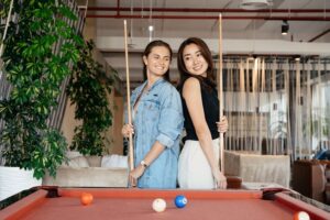 Two women standing side by side holding a pool cue
