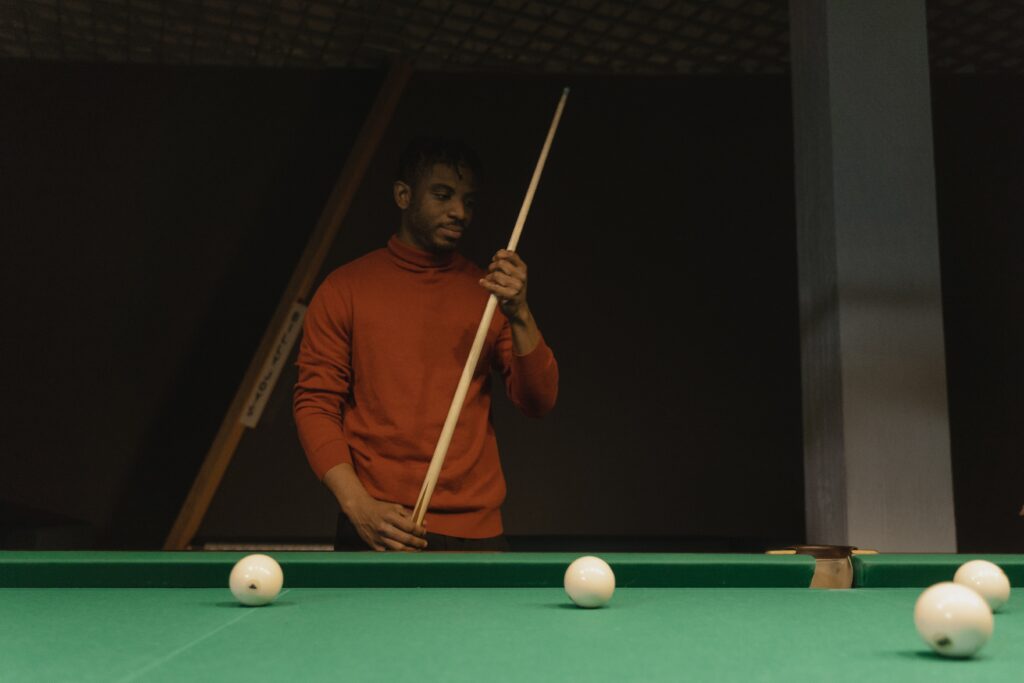 A person standing beside a pool table holding a cue