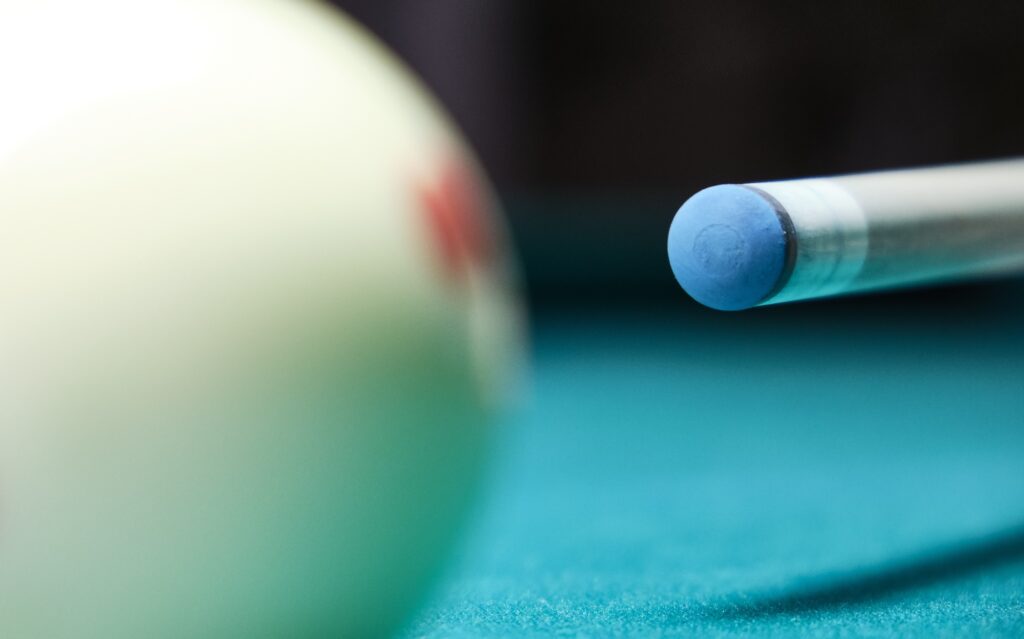 A close up shot of a tip of a cue and a white cue ball